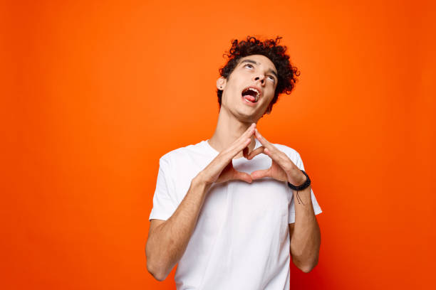 istock curly guy in a white t-shirt gesturing with his hand on an orange background 2140676759