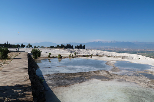 View from the travertine terraces of Pamukkale onto the valley with a paraglider in the background, Denizli, Turkey 2022