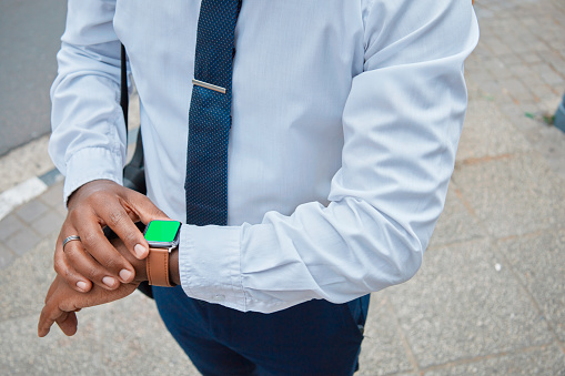 Close-up of a well-dressed African American businessman in a city setting looking at his smartwatch. The image conveys punctuality, technology, and urban lifestyle.