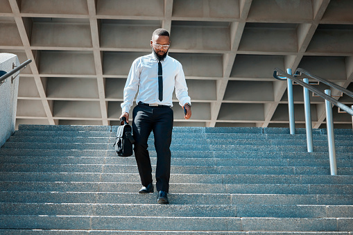 A professional black man in a suit walks down the stairs with ease, exuding confidence and determination. He carries a briefcase, symbolizing his business persona in a modern urban environment.