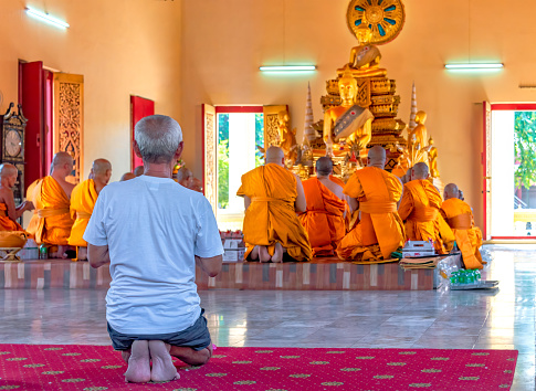 Wat Kaeng Khoi, Saraburi, Thailand, March 24,2024: Inside the chapel, an old man joins a group of monks to say the prayer before the lord Buddha.