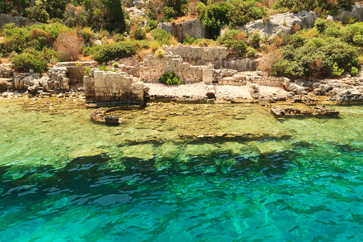 Submerged foundation in the foreground and structures onshore in the background at the ancient sunken city of Kekova, Kekova Island, Demre, Turkey 2022