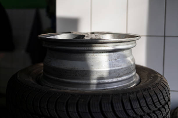 A close-up view of a silver car wheel rim showing damage, resting on a black tire in a workshop setting.