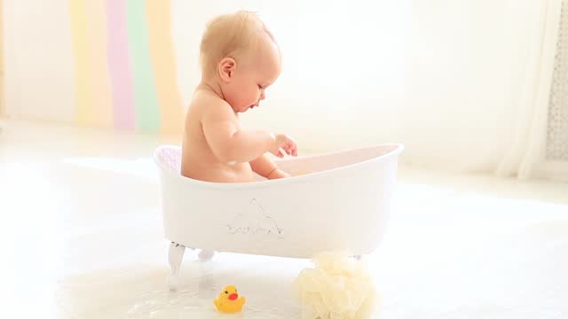 a little baby girl of six months is bathing in a bath with foam, soap is pinching the baby's eyes, bath foam got into the eyes of a child who is splashing in the water, the baby is washing