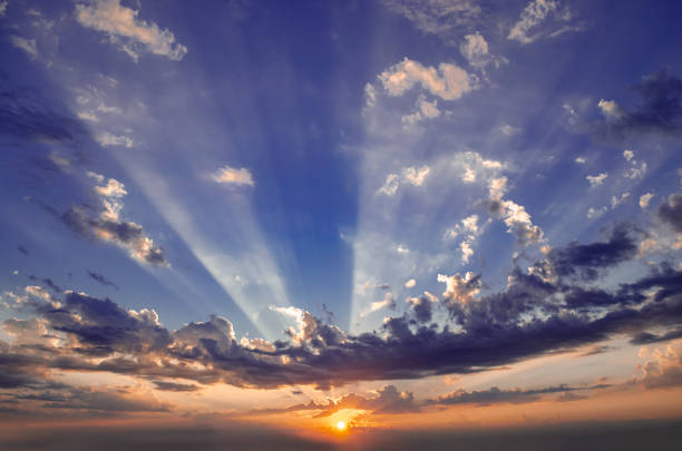 The sky is blue with a few clouds and the sun is setting. The sun is shining through the clouds, creating a beautiful and serene atmosphere
