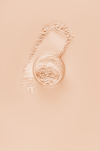 Loose light powder in a jar stands on a powder swatch. Brightening shade of beige tones. Concept of decorative cosmetics, makeup. Vertical view