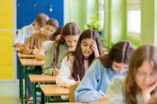Teenage girls sitting in a row at the desks in the classroom and writing an exam.