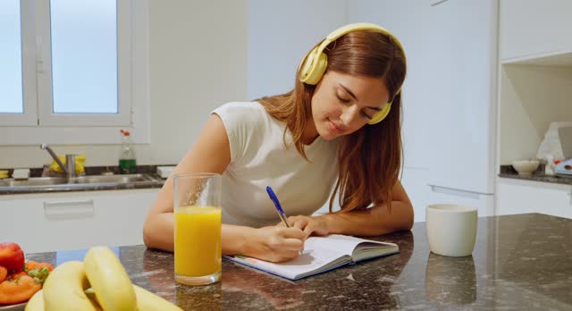 Young woman at home writing in a notebook while having a healthy breakfast