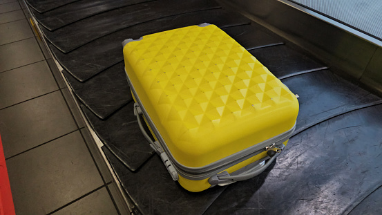 A yellow piece of luggage is stationary on top of a conveyor belt at an airport or transportation hub