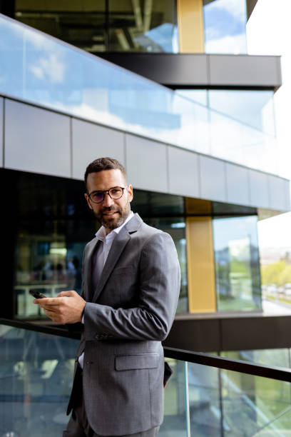 istock Confident Businessman Smiling in Sharp Suit Against Modern Glass Office Facade 2140891385