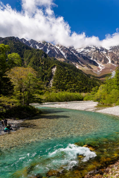 istock Hikers next to a clear river with snow-capped mountains in the background under a blue sky 2140900489