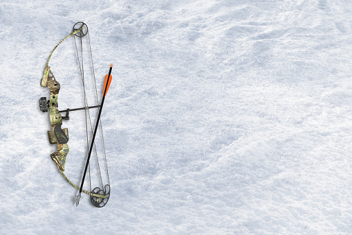 Camo hunting gear including bow and arrow on a snow background