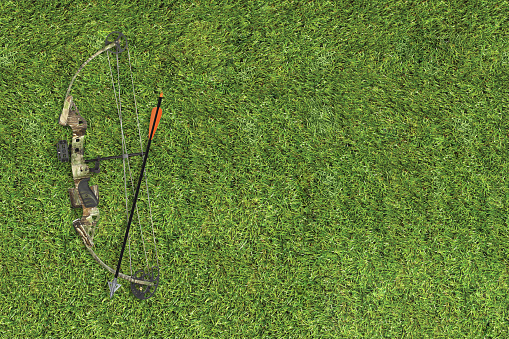 Camo hunting gear including bow and arrow laid on a grass background