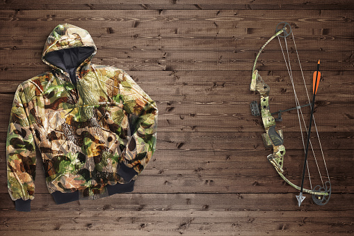 Camo hunting gear including bow and arrow and a camo jacket on a wood