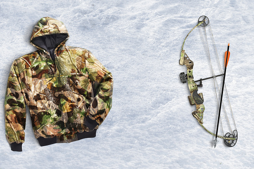 Camo hunting gear including bow and arrow and a camo jacket on snow