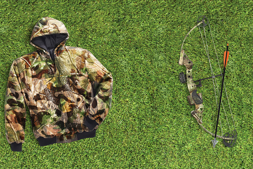 Camo hunting gear including bow and arrow and a camo jacket on grass