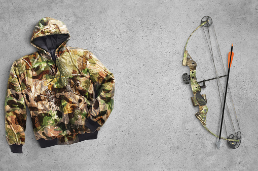 Camo hunting gear including bow and arrow and a camo jacket on a concrete