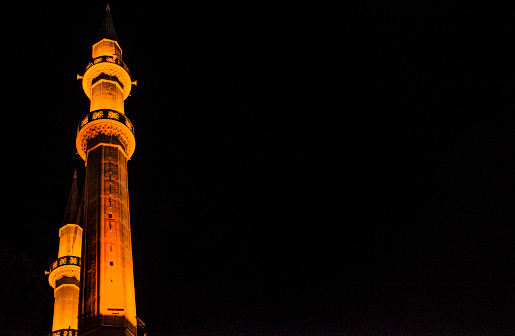 An enchanting view of a minaret with lights at night, illuminating the Islamic architecture and casting a serene glow on the urban landscape