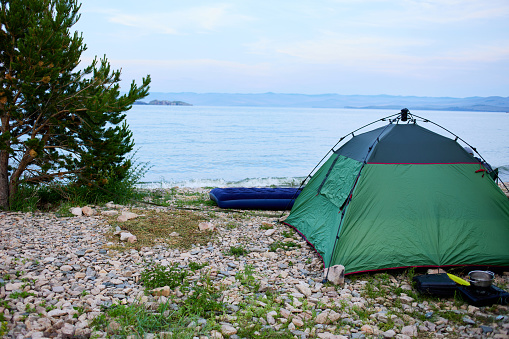 A tent on a pebble beach by the lake at dawn. A place for camping.