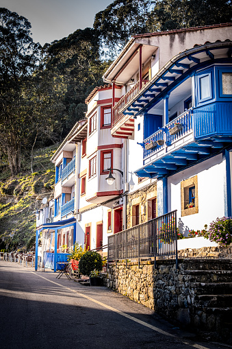 White houses line a rural street with vibrant blue and red balconies and orange rooftops.
