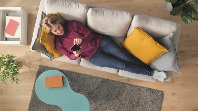 top down view of young woman on couch using smart phone vertical
