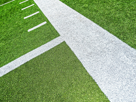 Bright green turf football field with white sidelines and yard line markings. Angled overhead view.