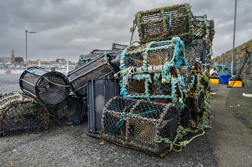 A pile of fishing gear is stacked on the ground. The scene is gloomy and overcast. The fishing gear is old and worn, and it appears to have been abandoned