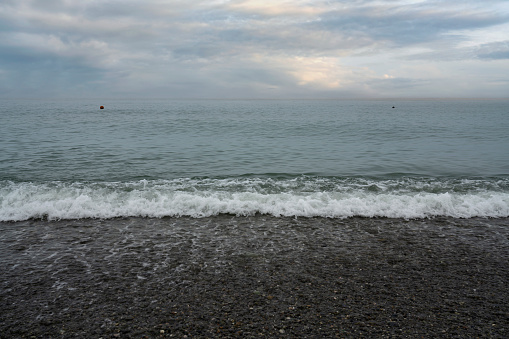 An incoming wave on the Black Sea and a pebble beach on the Sochi coast on a sunny summer day with clouds, Sochi, Krasnodar Territory, Russia