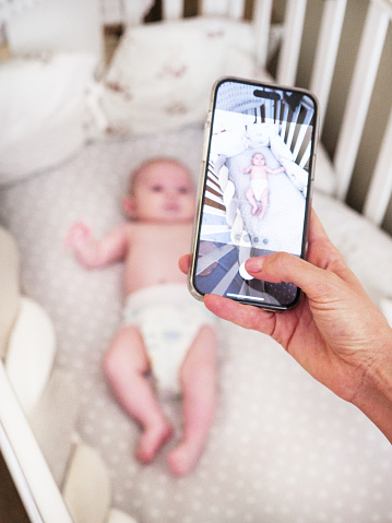 Mother taking photos of her infant daughter while she lying on the cradle