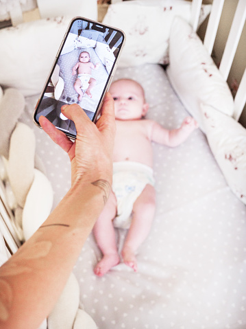 Mother taking photos of her infant daughter while she lying on the cradle