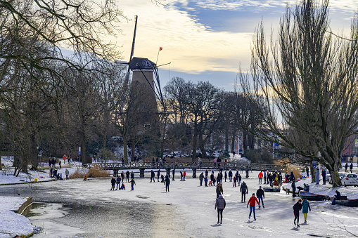 People skating on a canal in Alkmaar, Netherlands, with a windmill in the background