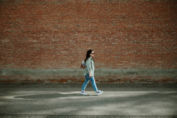 istock Woman walking by a red brick wall 2140996601