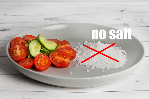 On a gray plate there is a mix of vegetables and a pile of sea salt, crossed out with a red cross. The inscription - no salt. Healthy eating concept.