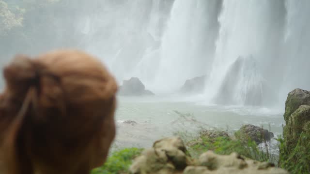 Unrecognizable Adventurous Woman Observing a Spectacular Waterfall in Nature During a Trip