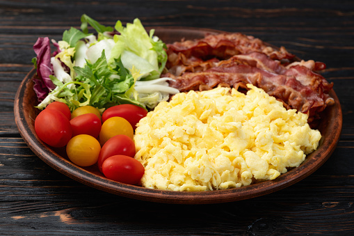 Breakfast plate . Scrambled eggs , bacon , cherry tomatoes and salad . Top view background