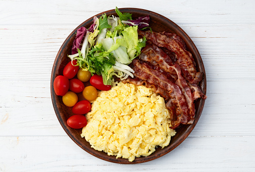 Breakfast plate . Scrambled eggs , bacon , cherry tomatoes and salad . Top view background