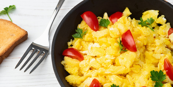Healthy vegetarian breakfast . Scrambled eggs in pan with cherry tomatoes and parsley . Top view