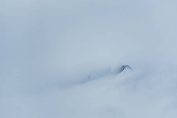 A massive mountain peak sticks out from the snow and the cloud cover near portal point on the antarctic peninsula.