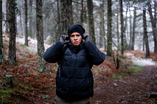 Latino adventurer dons gloves and hat in snowy Sierra de Guadarrama forest.