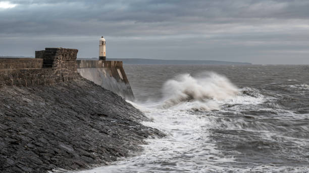istock Rough seas and waves crashing into a sea wall and lighthouse (Porthcawl, South Wales, UK) on a cloudy, winters day 2141108194