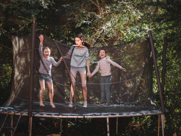 Three beautiful caucasian sister girls in jeans, shorts and a sleeved t-shirt jump on a trampoline Three beautiful caucasian sister girls in jeans, shorts and a sleeved t-shirt jump on a trampoline, frozen in happy with smiles on their faces in flight in the garden of a house among trees, close-up side view. Concept at home, home sports, happy childhood, children entertainment. funny camping signs pictures stock pictures, royalty-free photos & images