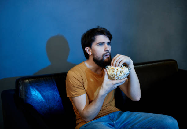 istock lonely man sitting on couch with popcorn plates gray wall 2141122580