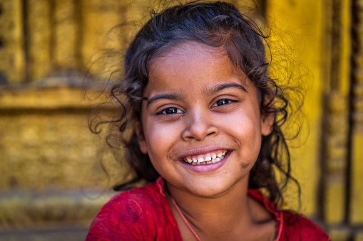 Portrait of little Nepali girl sitting in an ancient temple in Bhaktapur. Bhaktapur is an ancient town in the Kathmandu Valley and is listed as a World Heritage Site by UNESCO for its rich culture, temples, and wood, metal and stone artwork.