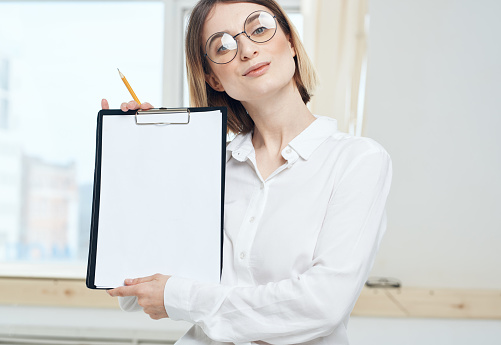 A woman is holding a folder with a white sheet of mockup paper. High quality photo