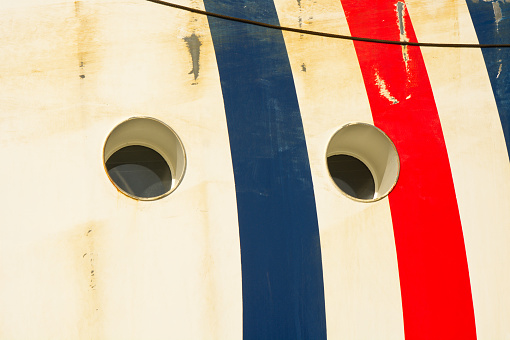 Two portholes in ships hull with white, blue and red stripes