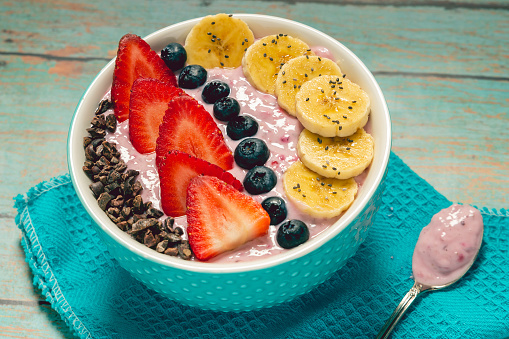 colorful fruit bowl with strawberries, blueberries, bananas and cacao nibs on yogurt  base