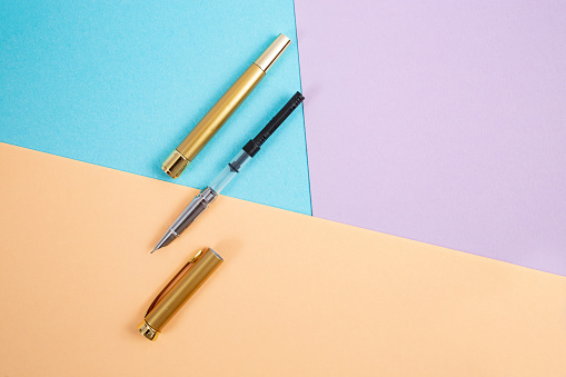 Opened golden fountain pen on cream, blue and purple background,
