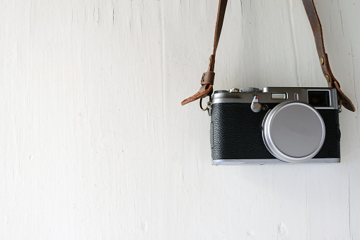 Vintage film camera with leather strap on rustic white background with Copy Space.
