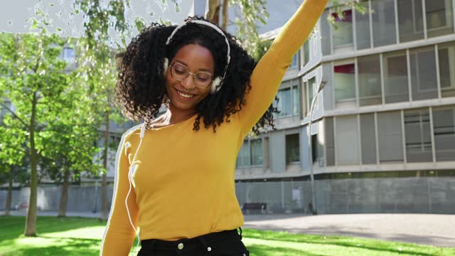 Smiling young African American woman dancing to music on her smartphone outdoors