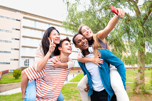 Young students piggybacking their fellow college students on campus. Excited friends posing for a funny photo.